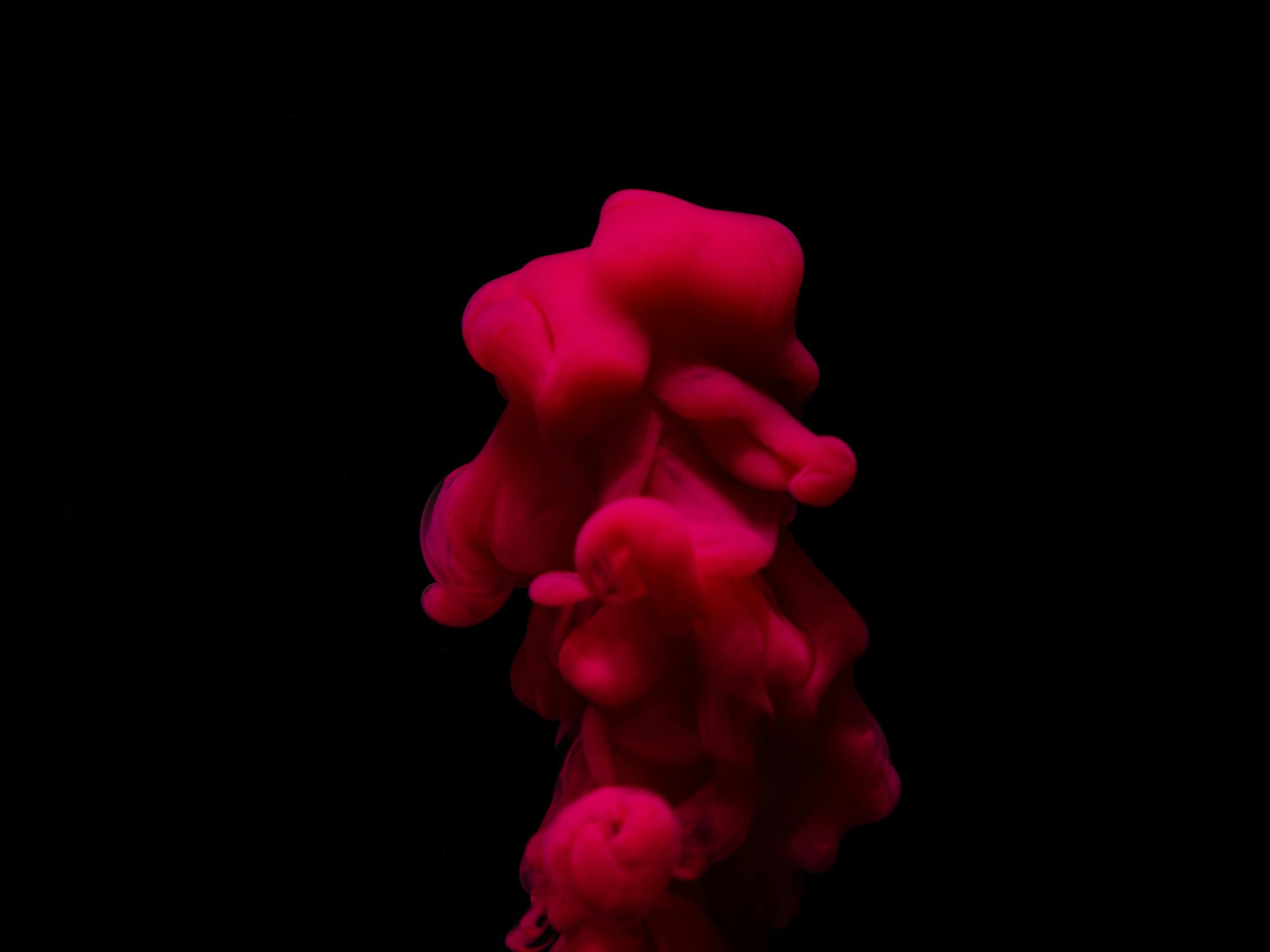 A vivid red ink swirl submerged in water against a black background, creating an artistic abstract effect.