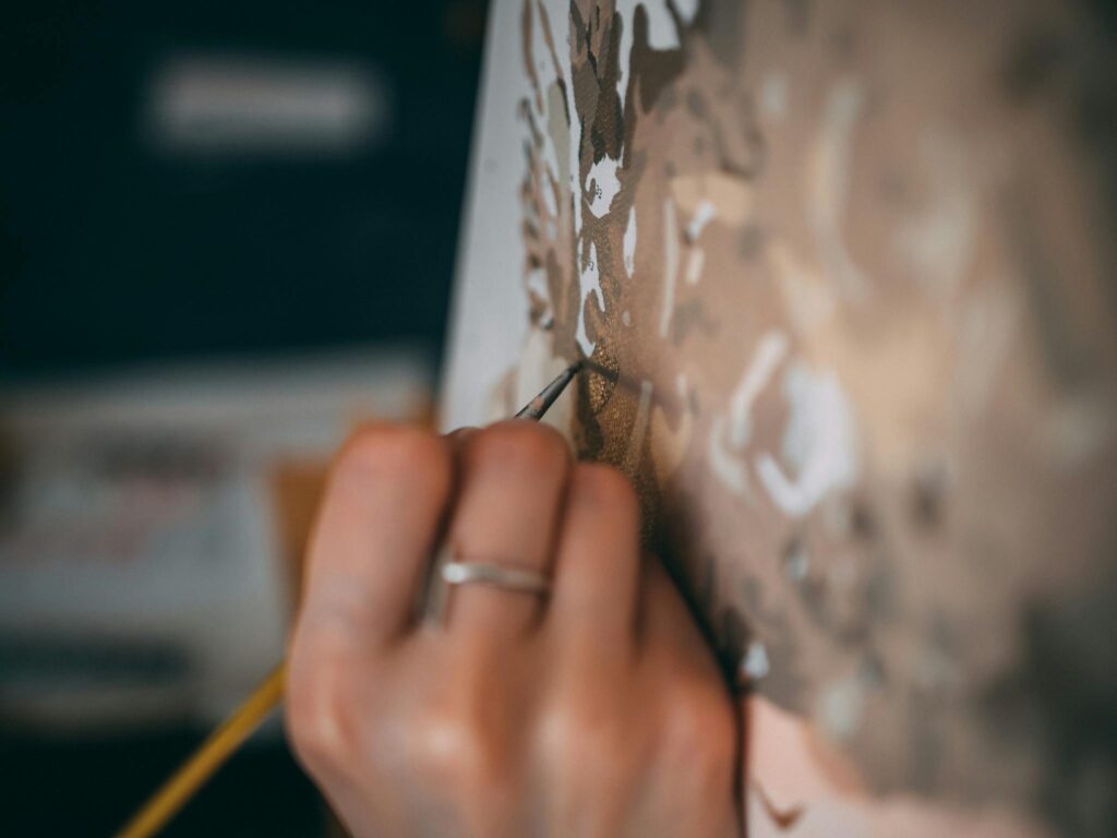 Artistic close-up of a hand painting details on a canvas with a paintbrush.